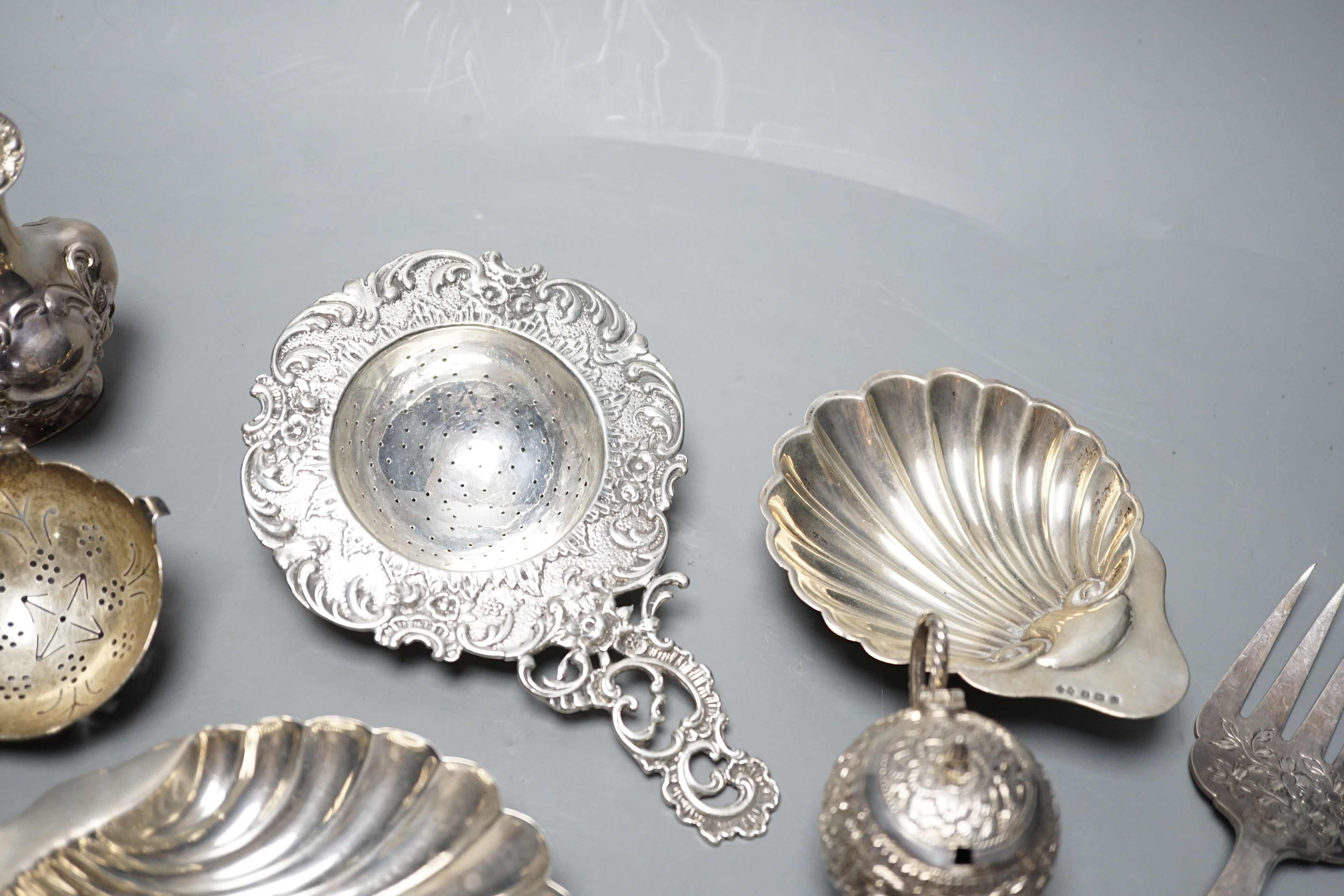 Small silver including two butter shells, a continental silver tea strainer, English tea strainer, pair of salts, swizzle stick, serving fork, two pepperettes and an Indian white metal three piece condiment set.